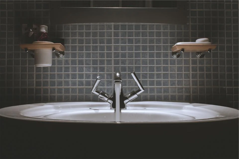 Bathroom sink and faucet in front of a grey tiled wall