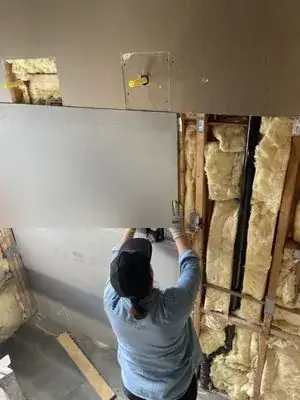 Cement backer board being installed on a shower wall over insulated framing