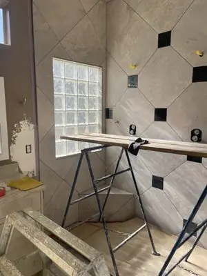 Diagonal shower wall tile with black accent squares being installed