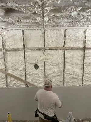 Spray foam insulation in an open wall while new drywall goes up
